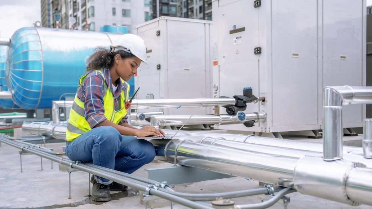 A woman working on air ducts on the exterior of a building