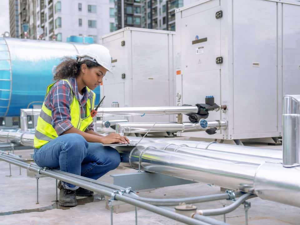 A woman working on air ducts on the exterior of a building